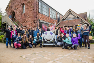 A large group of young people taking part in the Environmental Leadership Programme, stood outside an old building. They are smiling at the camera